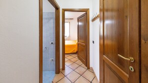 Ein Flur mit Fliesenboden, Holztüren und einem Bett im Hintergrund.