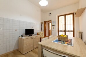 Une cuisine avec un mur recouvert de carreaux, un meuble en bois, une télévision, une table à manger avec un set de table et un panier en osier contenant des citrons.
