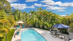 Une piscine entourée d’une végétation luxuriante et de palmiers, avec des chaises longues et des parasols à proximité.