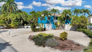 Un bâtiment bleu avec une porte de garage blanche, entouré de palmiers et d’un jardin bien entretenu.