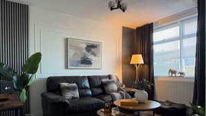 A modern living room with a black leather sofa, a coffee table, a lamp, and a painting on the wall.