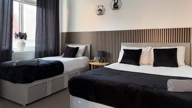 A hotel room with two beds, a window with curtains, a potted plant, and a wall-mounted clock.