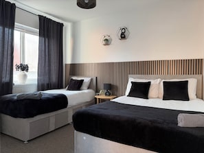 A hotel room with two beds, a window with curtains, a potted plant, and a wall-mounted clock. - Luxury Modern Home | Sleeps 10 | Generous Kitchen & Lounge (Leeds)