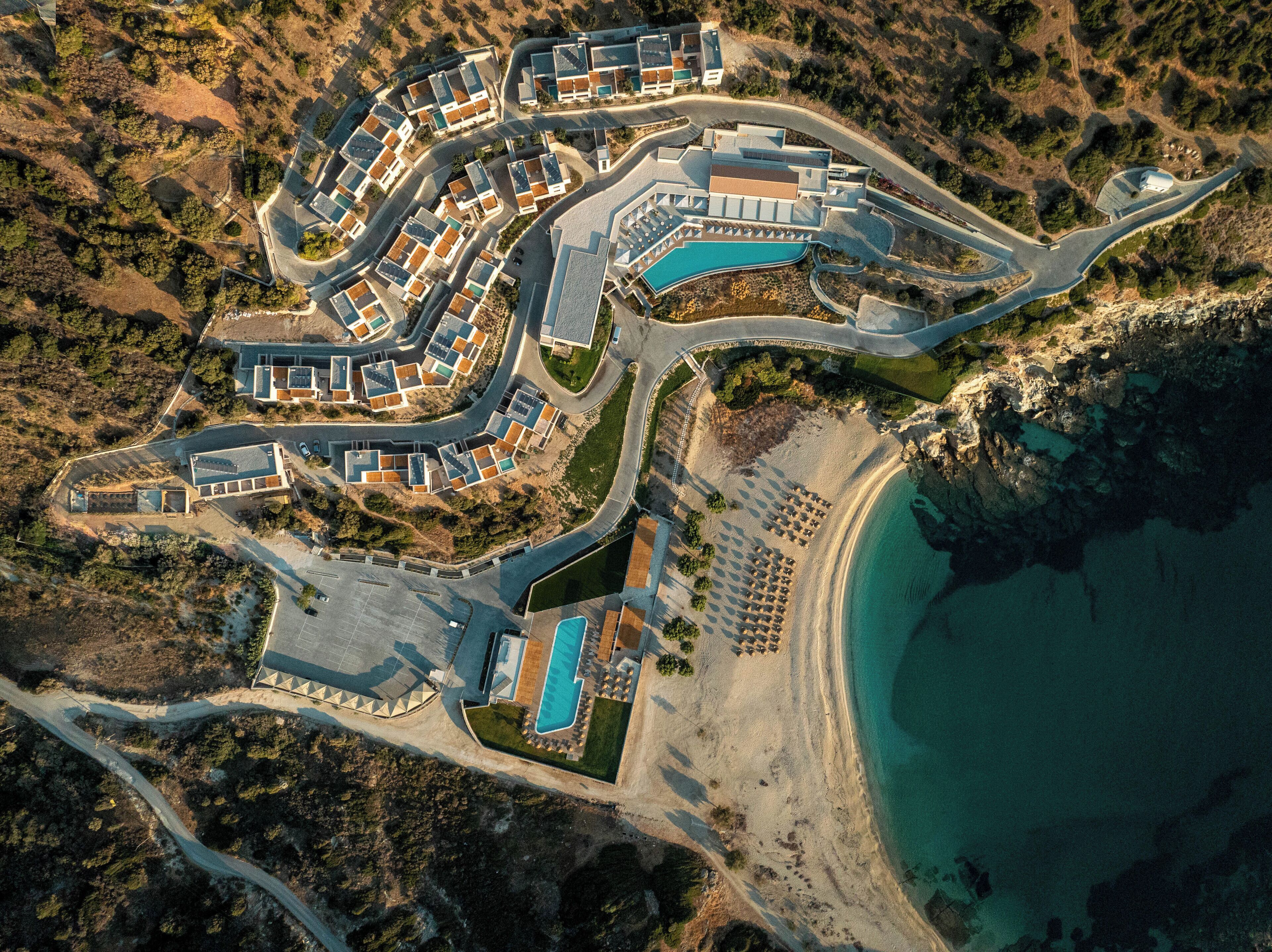 Eine Luftaufnahme eines Küstenresorts mit mehreren Gebäuden, einem Swimmingpool und einem Strand.