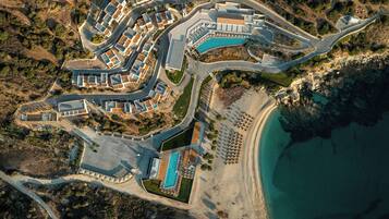 Vista aérea de un complejo turístico costero con varias edificaciones, una piscina y una playa.