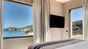 A bedroom with a large window offering a view of a beach and rocky landscape. - Heromylos Resort And Spa (Kymi-Aliveri)