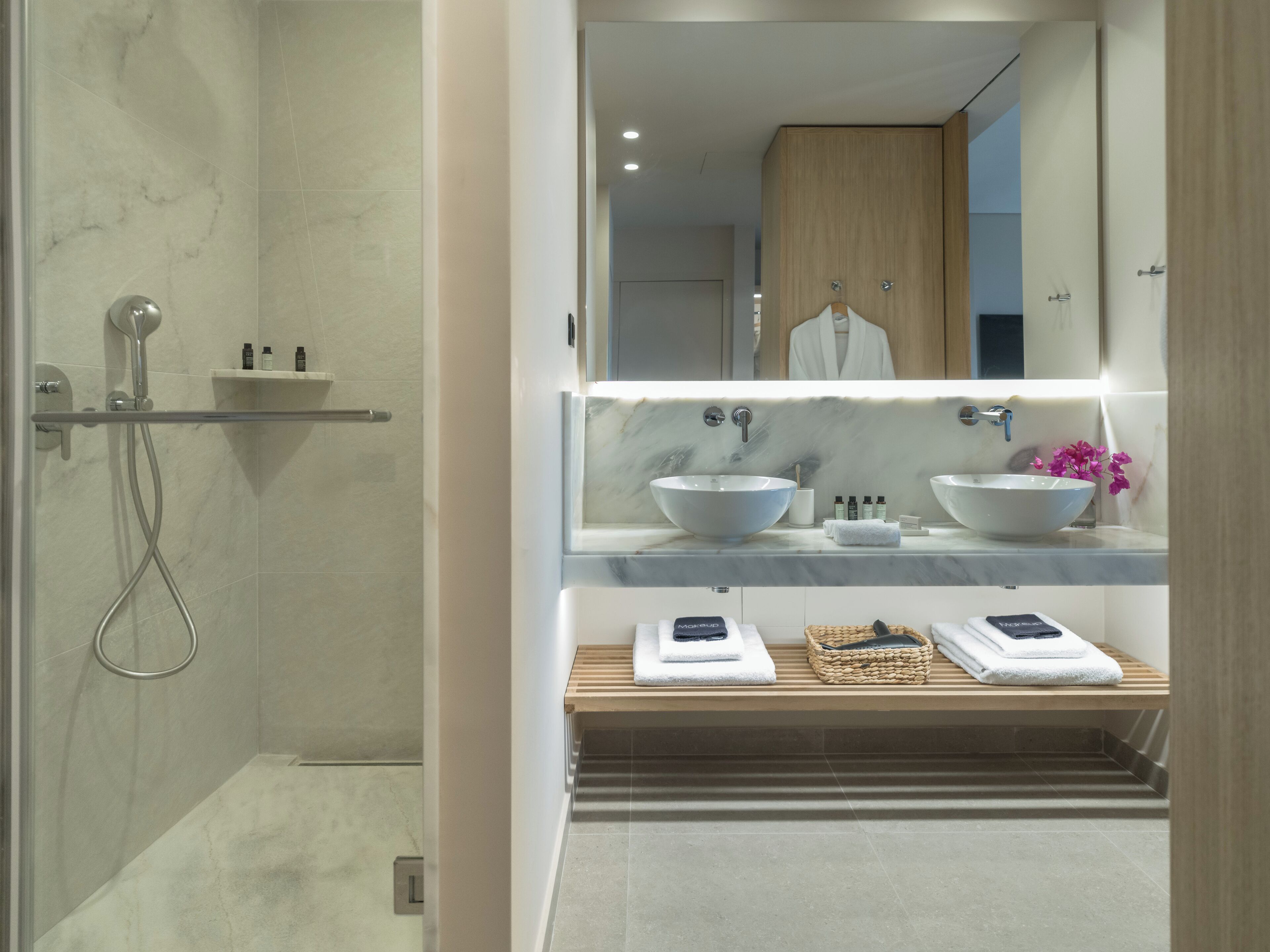 A modern bathroom with a walk-in shower, two sinks, and a vanity with a mirror.