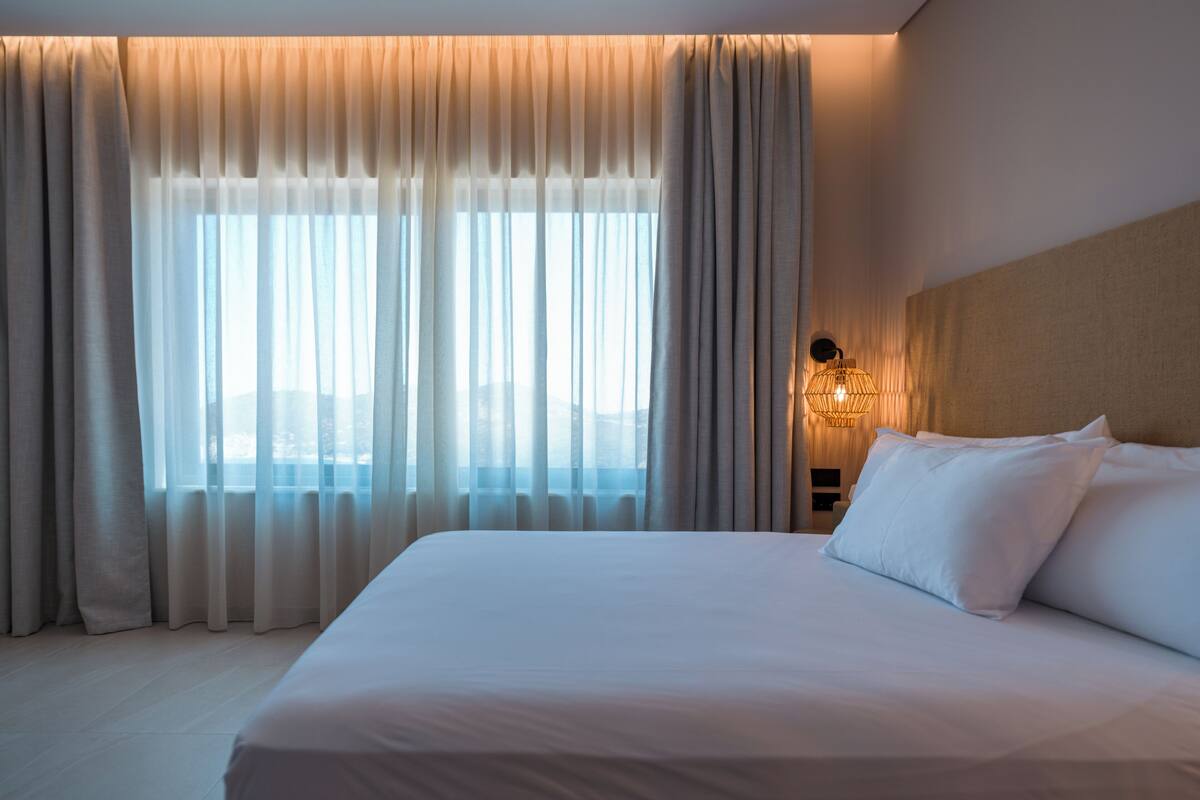 Una habitación de hotel con una cama grande, cortinas, una mesita de noche y una lámpara de pared.
