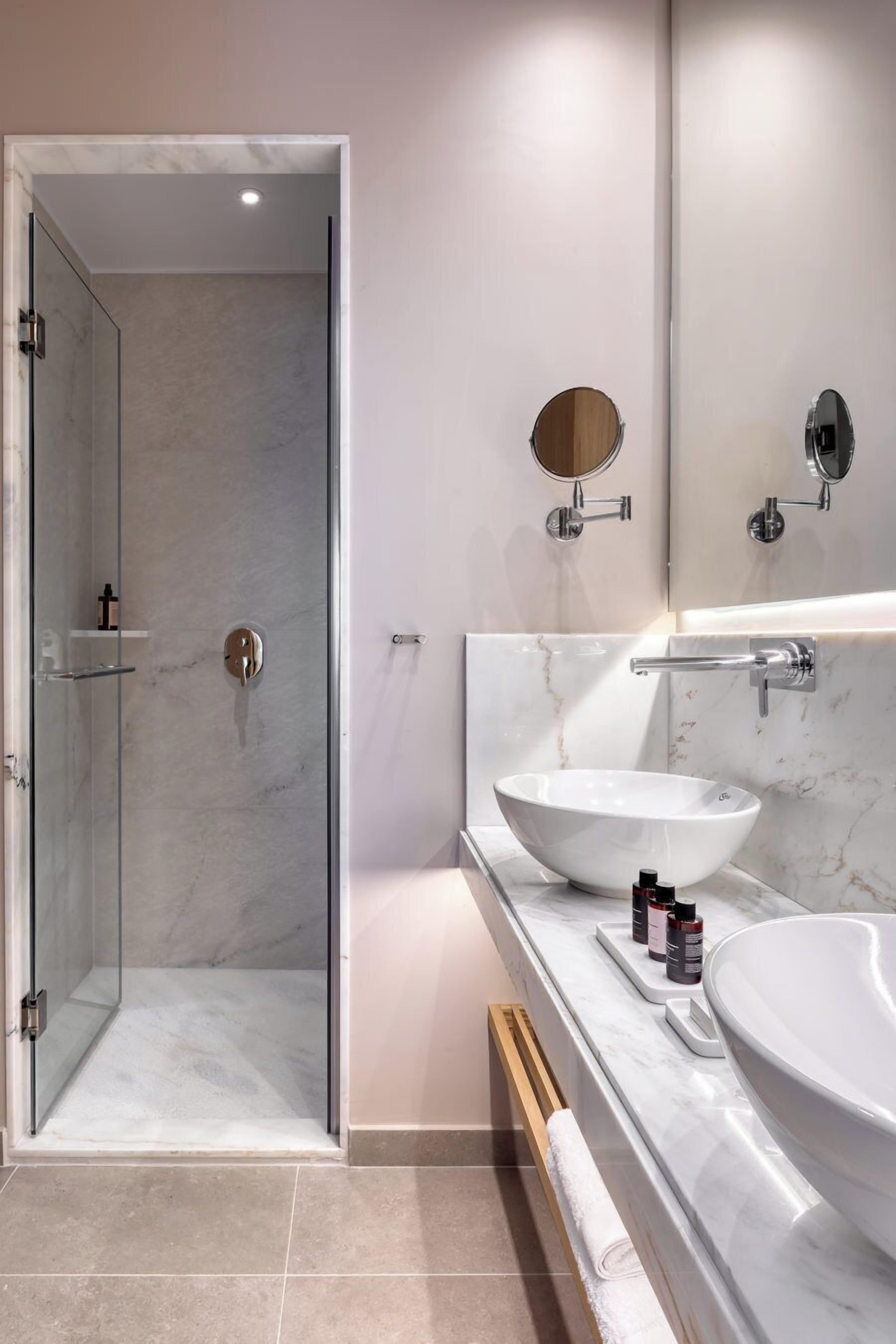 Un baño moderno con ducha envuelta en vidrio, un lavamanos grande de color blanco y un espejo sobre el tocador.