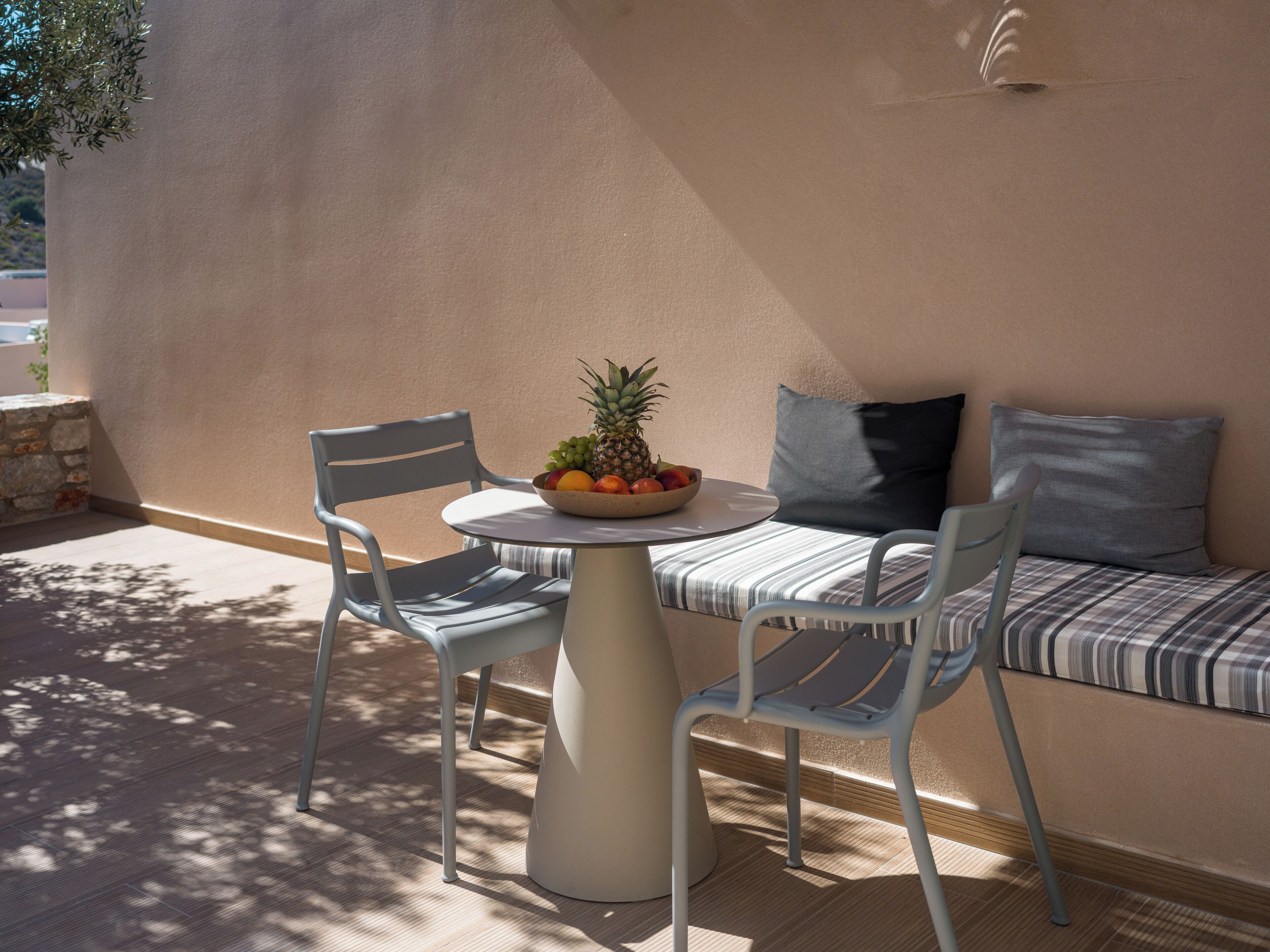 A sunlit outdoor seating area with a round table, two chairs, and a bowl of fruit.