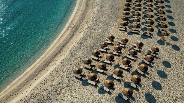 An aerial view of a beach with rows of sun loungers and umbrellas aligned parallel to the shoreline. - Heromylos Resort And Spa (Kymi-Aliveri)
