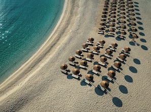 An aerial view of a beach with rows of sun loungers and umbrellas aligned parallel to the shoreline.
