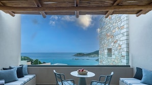 A balcony with a stone wall, a table with chairs, and a view of the sea. - Heromylos Resort And Spa (Kymi-Aliveri)