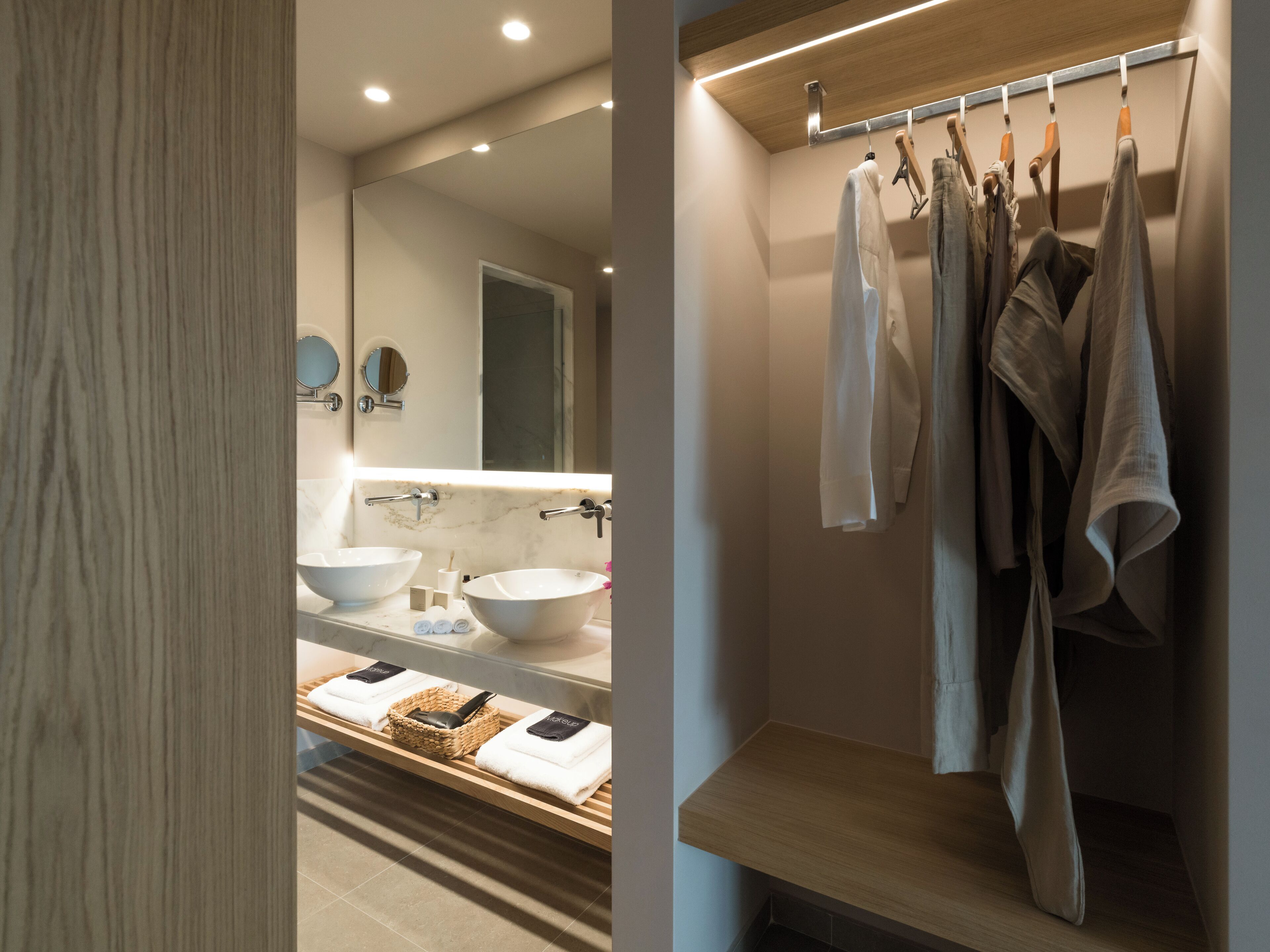 Un baño moderno con un espejo grande, dos lavamanos y un perchero con varias toallas.