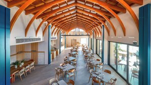 A spacious dining area with high wooden beams and large windows. - Heromylos Resort And Spa (Kymi-Aliveri)