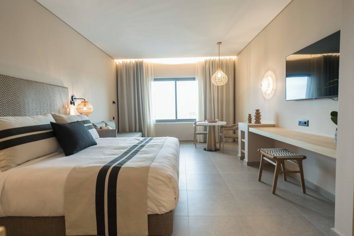 Una habitación de hotel moderna con una cama grande, un escritorio, una silla, un televisor y una ventana con cortinas.