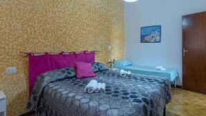 Une chambre avec un mur à motifs, un lit avec des serviettes roulées, une table de chevet, un tableau et une porte en bois.