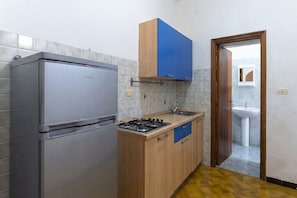 A compact kitchen with a stainless steel refrigerator, a gas stove, wooden cabinets, and a sink.