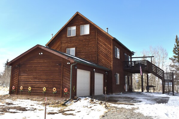 A two-story wooden cabin with a garage, a covered porch, and a small outdoor area with a fire pit. - Sunflower Cabin • Modern Family Retreat • Easy Access • Pets OK • 1.2 Acres (Jefferson)
