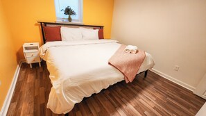 Ein Schlafzimmer mit einem Bett, einem Nachttisch, einem Fenster mit Jalousien und einem Blumentopf auf dem Fensterbrett.