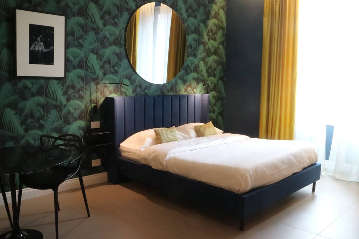 A bedroom with a bed, a chair, a mirror, and a wall with a leaf pattern.