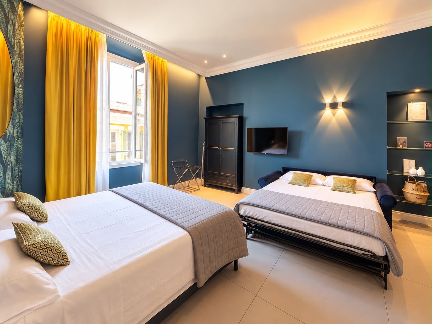 A hotel room with two beds, a wardrobe, a television, and a shelf with decorative items.