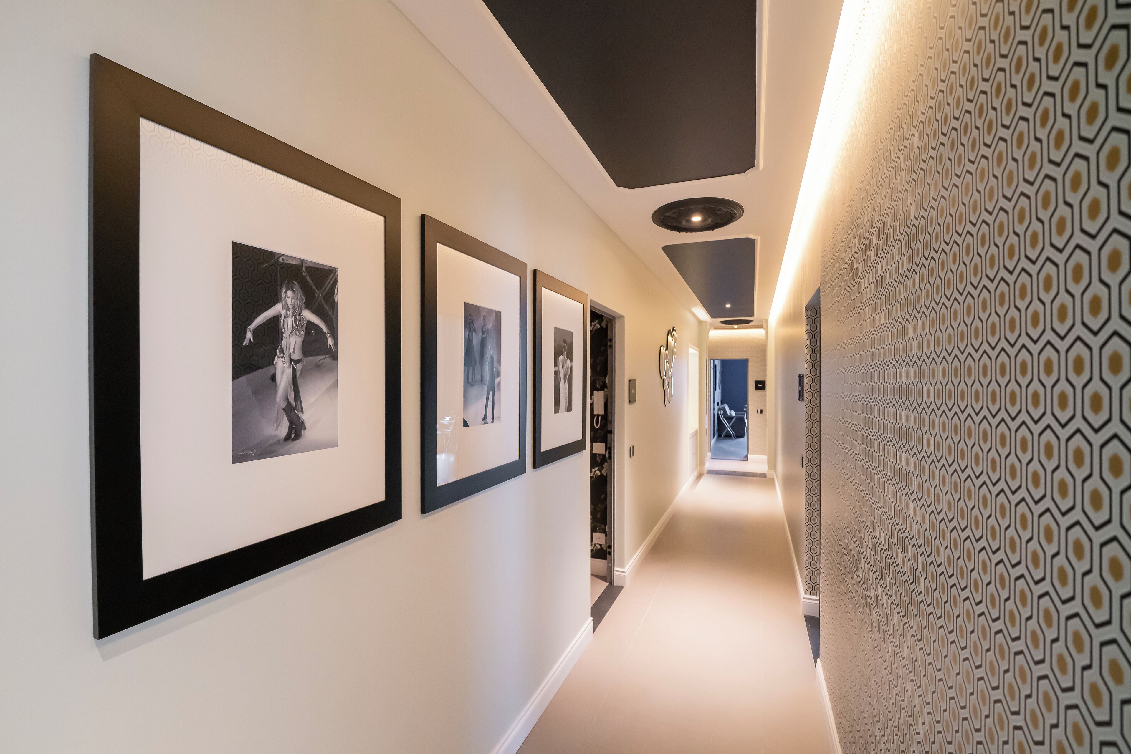 A hallway with framed photographs on the wall, a patterned wall on the right, and a door at the end.