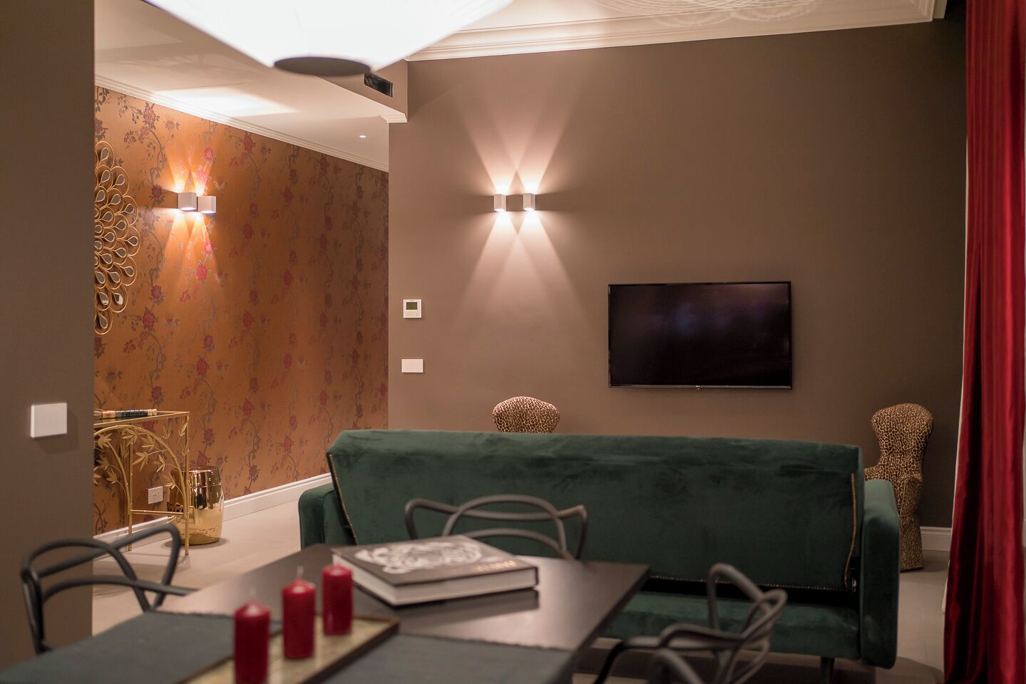 Un comedor con un sofá verde, una mesa con velas y un televisor montado en la pared.