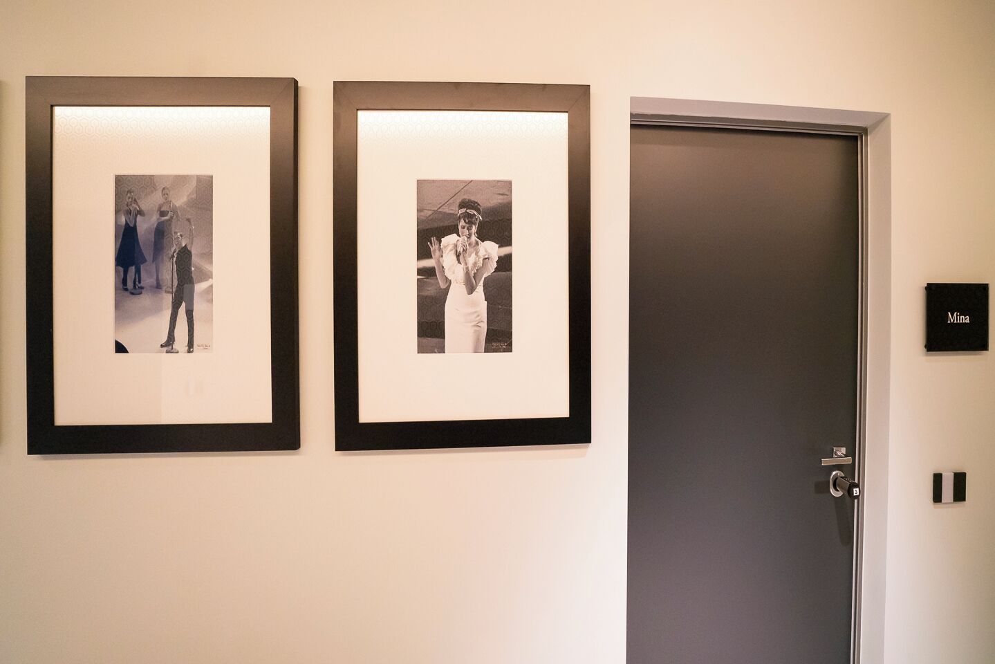 Two framed photographs on a wall, a door with a nameplate, and a light switch.