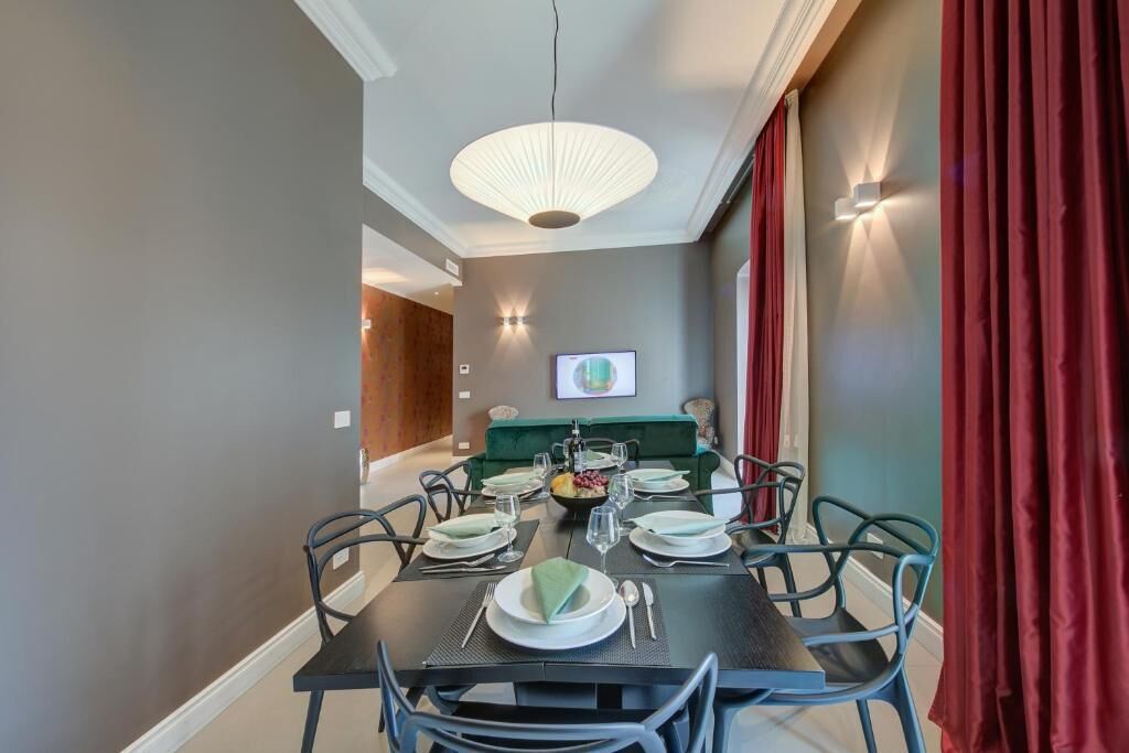 A dining area with a dark table set for six, surrounded by chairs, a green sofa, and a wall-mounted TV.