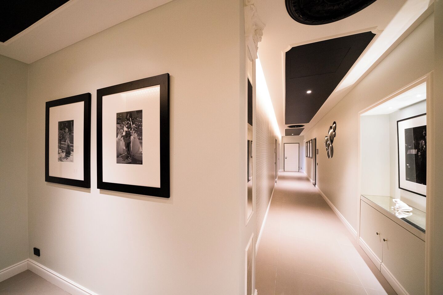 Ein Flur mit gerahmten Schwarzweißfotos an der linken Wand, eine lange Diele mit einer reflektierenden Oberfläche auf der rechten Seite und einer Tür am Ende.