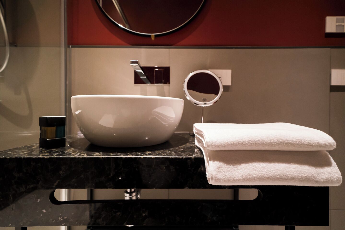 A bathroom with a large white basin, a round mirror, and a folded white towel on the counter.