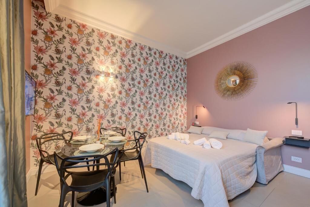 A bedroom with a bed, bedside table, and a wall with floral wallpaper.