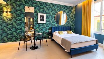 A bedroom with a bed, a dining table with chairs, a mirror, and a wall with a leafy pattern.