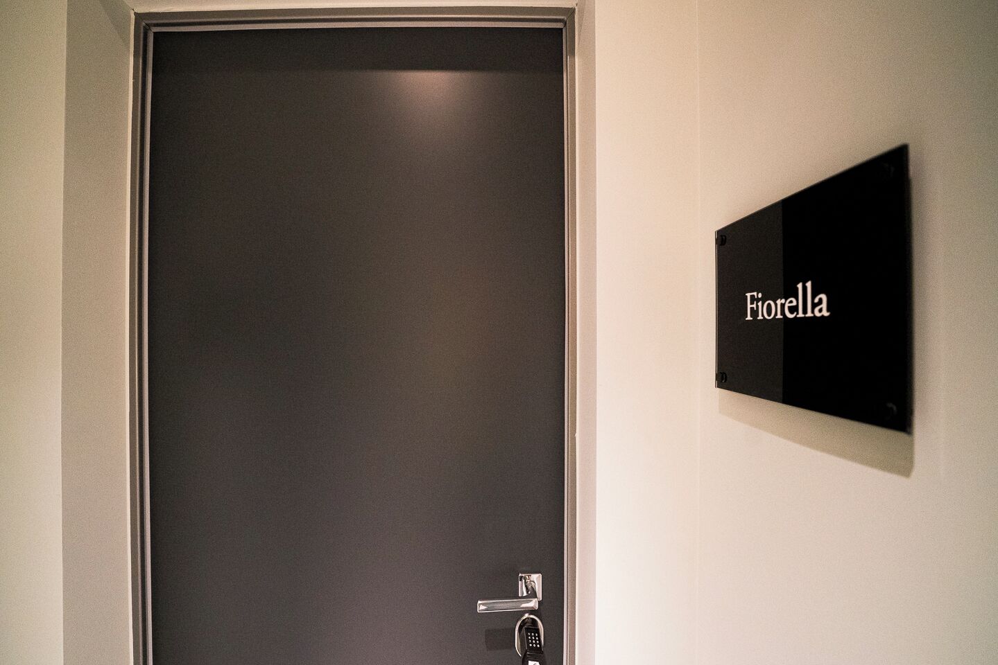En stängd dörr med ett digitalt lås och en skylt med texten ”Fiorella” på väggen.
