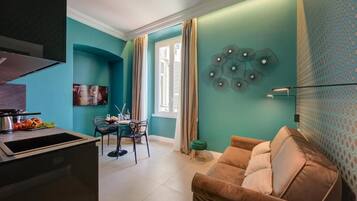 A modern living room with teal walls, a brown sofa, a dining area with a table and chairs, and a kitchen with a sink and stove.