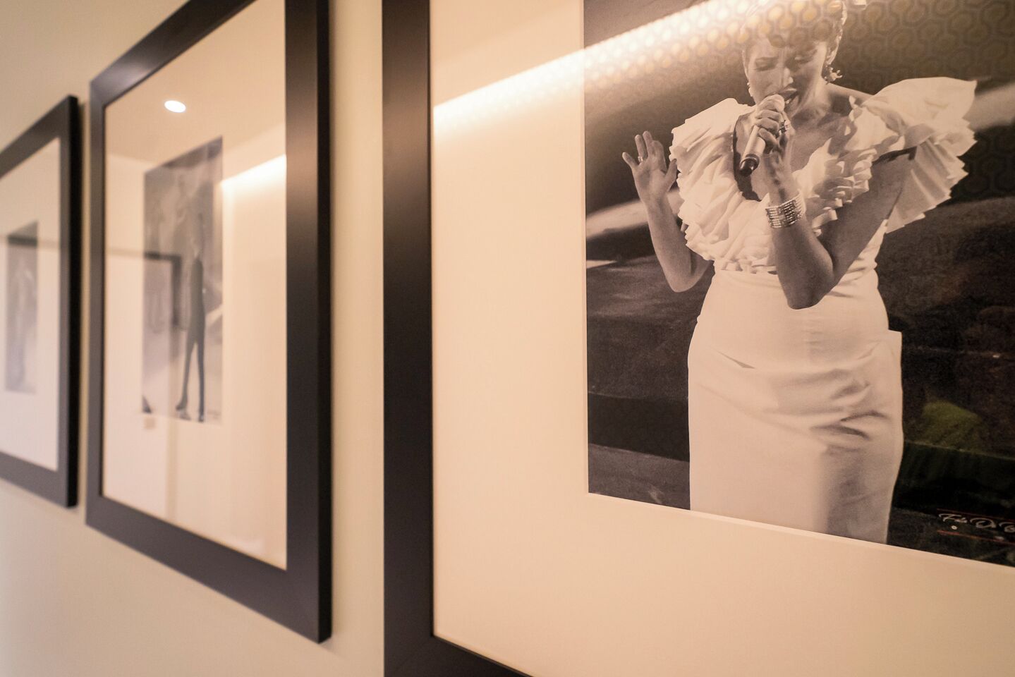 A wall with framed photographs and a single large framed photo of a person in a white dress.