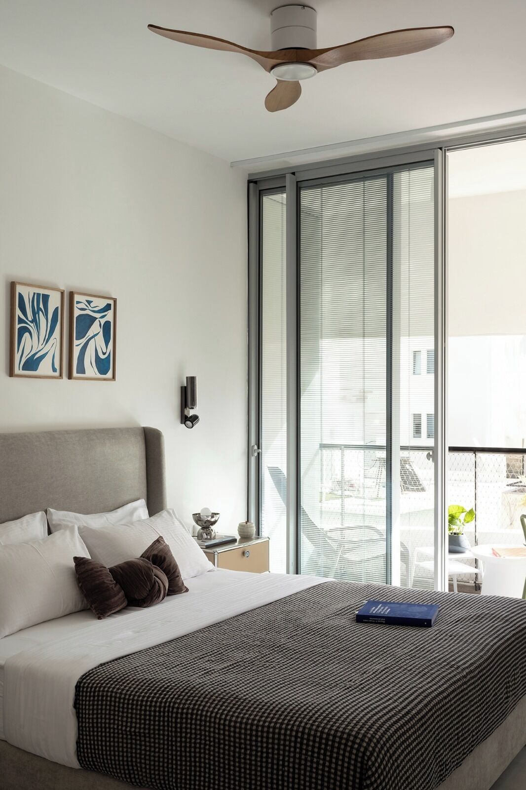 A modern hotel room with a large bed, a ceiling fan, and a view of the city through floor-to-ceiling windows.