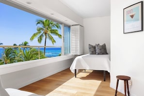 Ein Schlafzimmer mit großem Fenster mit Blick auf einen Strand, einem Bett mit weißer Bettdecke und einem gerahmten Bild an der Wand.