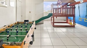 A room with a foosball table, a slide, and a play area with a wooden structure and swings. - Oceana Suites Estacion Central (Santiago)