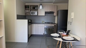 Uma cozinha compacta com micro-ondas, fogão e frigorífico. Há uma mesa de jantar com pratos e talheres.