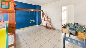Een kamer met een tafelvoetbaltafel, een klimladder en een schommelset tegen een blauwe muur.