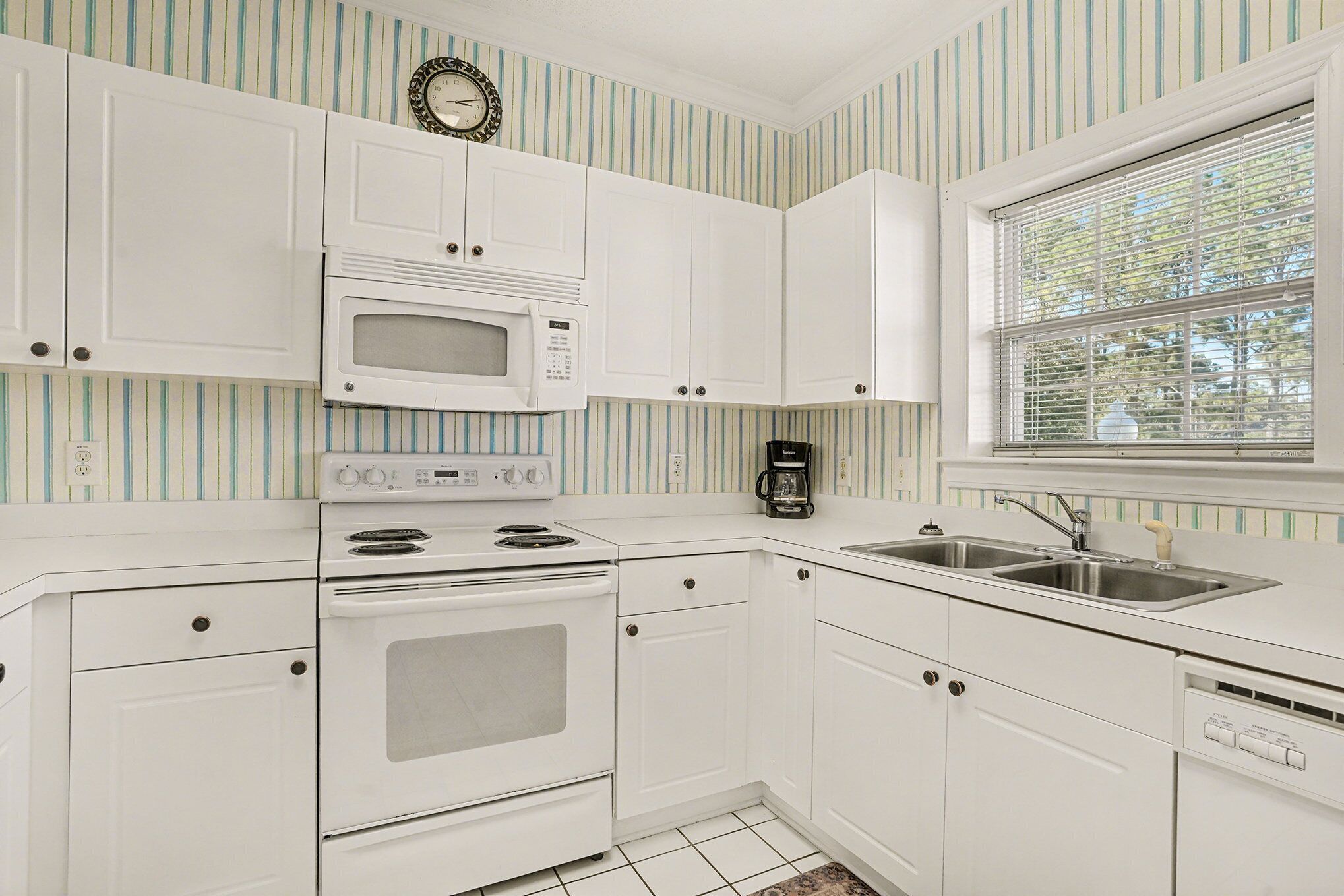 A kitchen with white cabinets, a microwave, stove, and a sink.