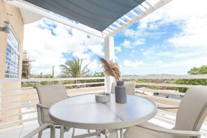 Une table ronde avec deux chaises, un vase et une bougie, sur un balcon doté d’une balustrade blanche et offrant une vue sur le paysage.