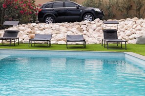 Une piscine avec des chaises longues et un SUV noir garé derrière un muret en pierre.