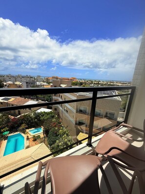 A balcony with a view of a swimming pool, buildings, and a clear sky.