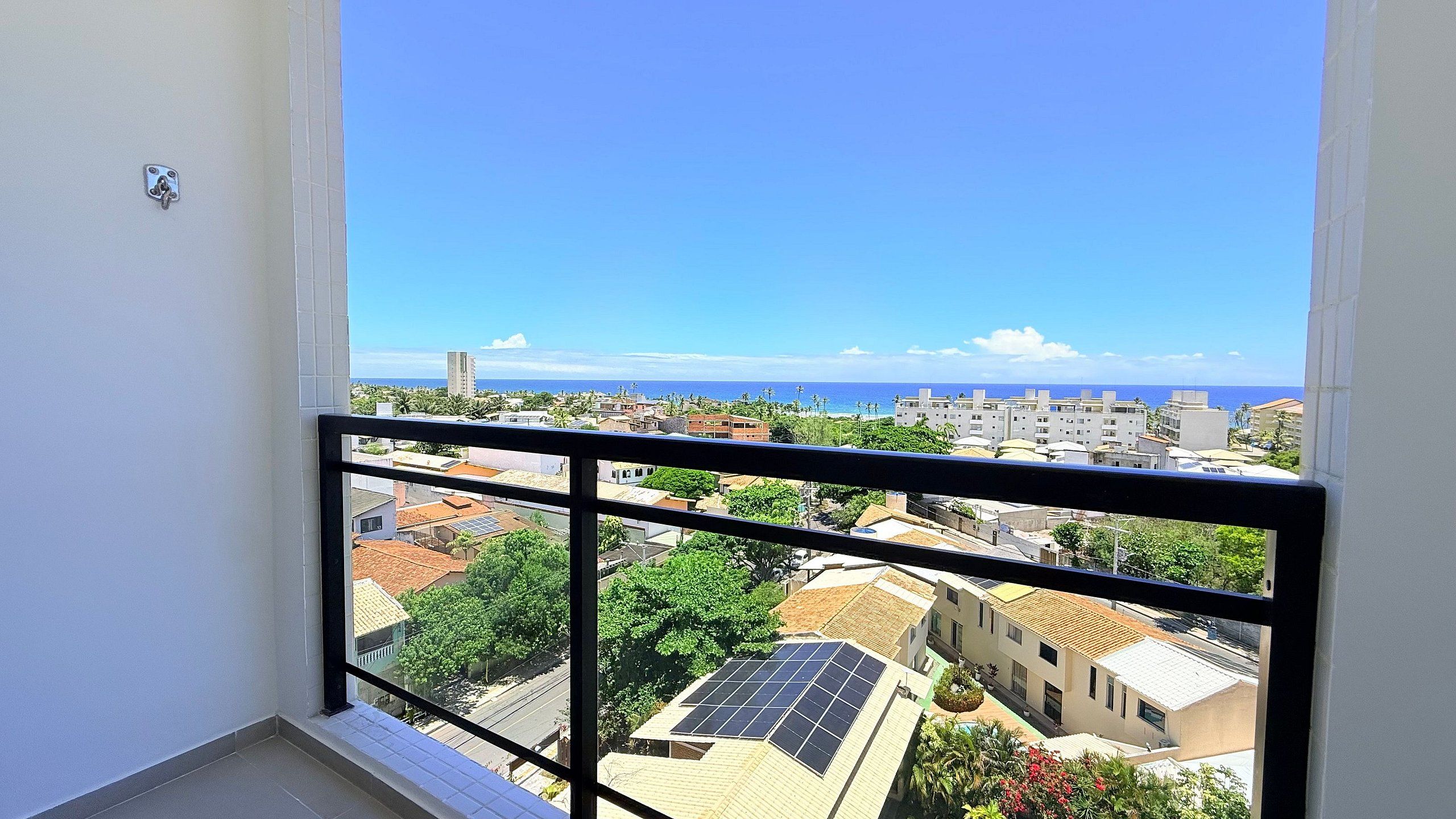 Un balcon offrant une vue sur un paysage urbain côtier, avec des bâtiments et un ciel bleu dégagé.