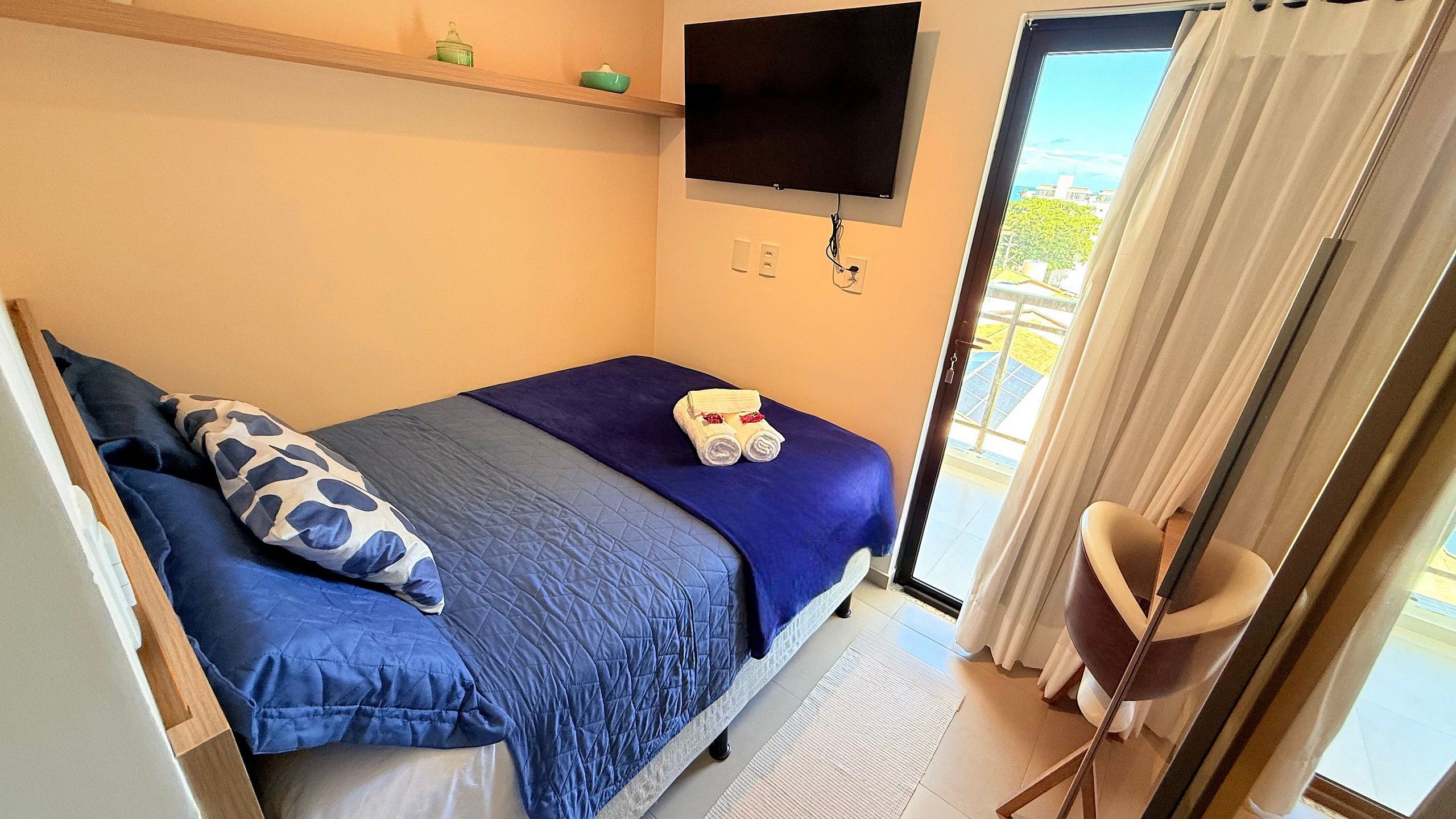 A bedroom with a bed, pillows, a TV, and a view of the outside.