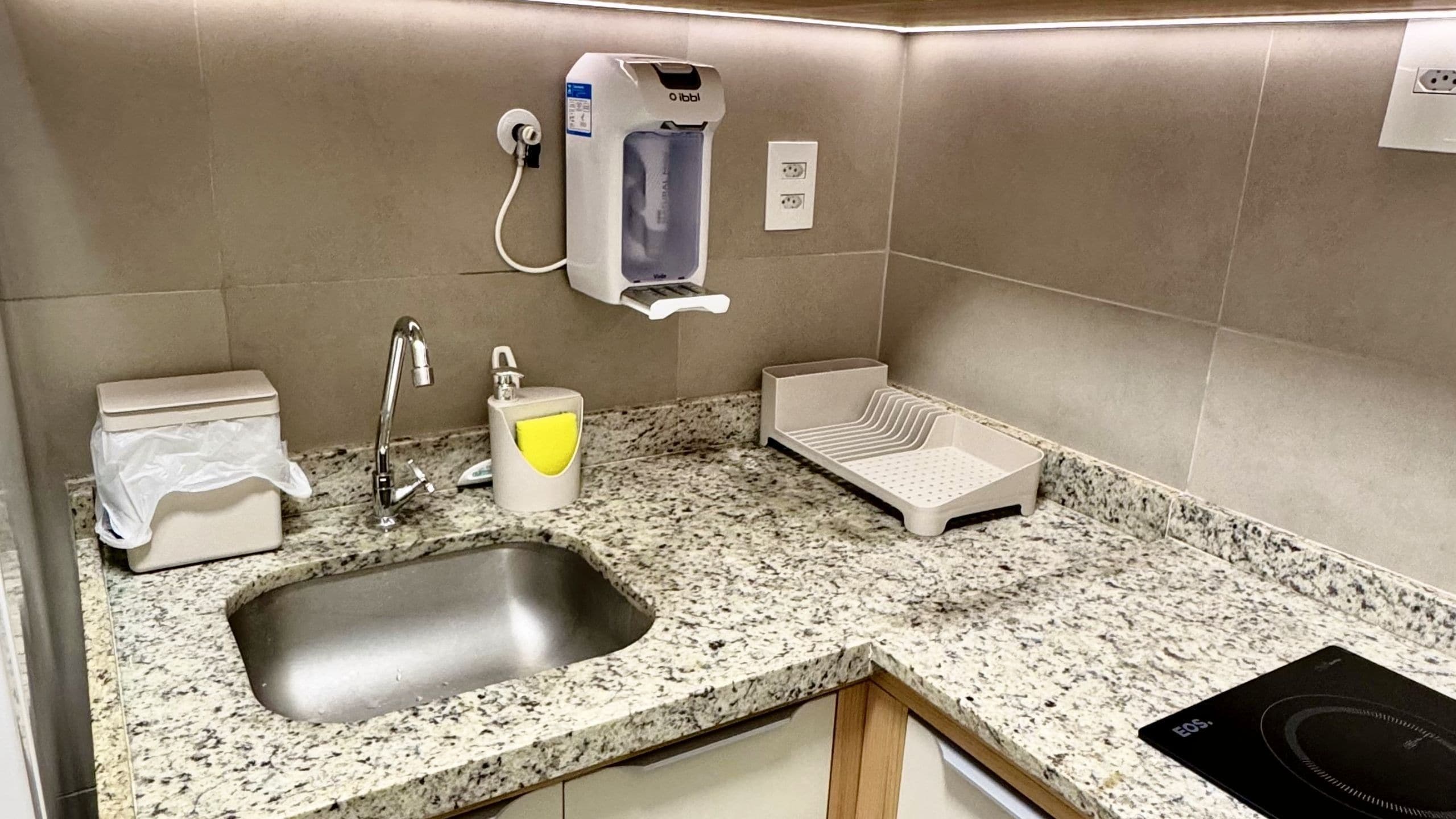 Casa de banho com bancada de granito, lavatório, sanita, secador de mãos e dispensador de papel.