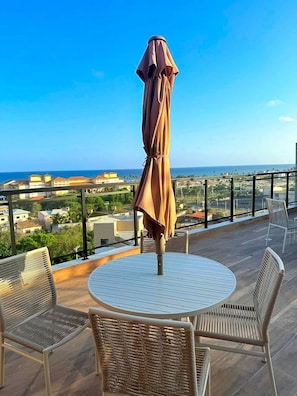 A balcony with a round table and wicker chairs, overlooking a coastal view. - Concept Life Stella (Salvador)